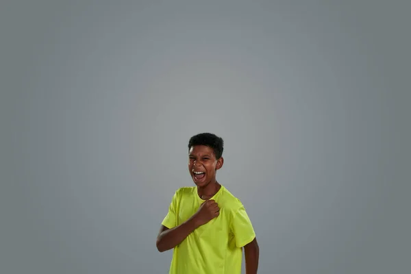Stop nooit. opgewonden tiener afrikaanse jongen dragen neon t shirt houden vuist op zijn borst en schreeuwen terwijl staan tegen grijze achtergrond — Stockfoto