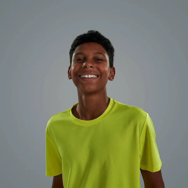 Genç sporcu, mutlu, neon tişört giyen Afrikalı bir gencin portresi stüdyoda gri arka planda kameraya gülümsüyor. — Stok fotoğraf
