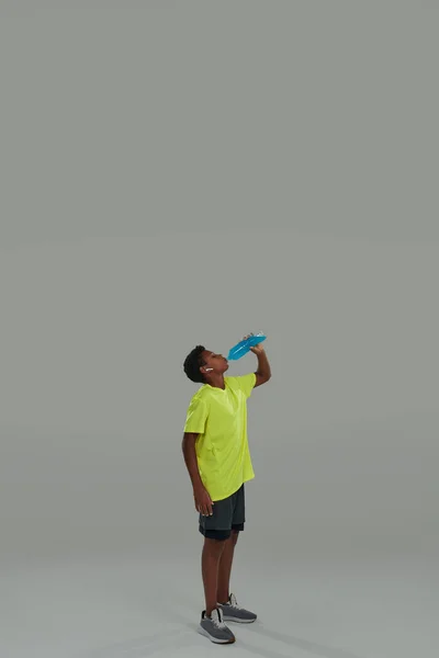 Verfrissend na de training. verticaal schot van een sportieve tiener afrikaanse jongen met blauwe energie drankje terwijl staande tegen een grijze achtergrond — Stockfoto