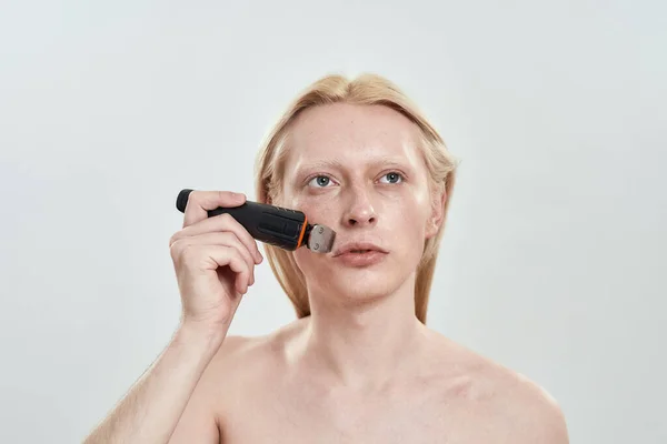 Homem caucasiano jovem usando cortador sem fio na barba — Fotografia de Stock