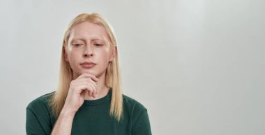 Uzun sarı saçlı, beyaz, genç bir adam aşağıya bakıyor.