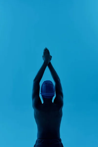 Visão traseira de um menino africano adolescente em pé boné natação em pose inicial isolado sobre fundo azul, pronto para mergulhar — Fotografia de Stock