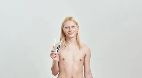 Young caucasian blond man holding different toothbrushes in hand — Stock Photo, Image