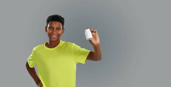 Encantado adolescente africano mostrando um recipiente de drogas médicas na câmera, sorrindo alegremente enquanto estava de pé contra fundo cinza no estúdio, bandeira panorâmica — Fotografia de Stock