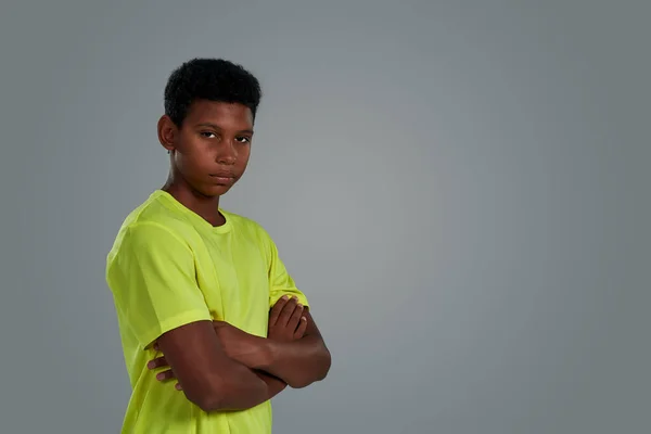 Confiado adolescente africano niño en camiseta de neón mantener los brazos cruzados, mirando a la cámara mientras posando aislado sobre fondo gris, banner web — Foto de Stock