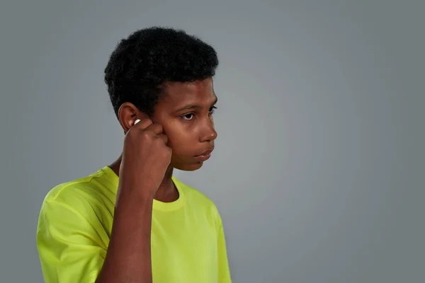 Genç Afrikalı çocuk gri arka planda dururken kablosuz kulaklık ayarlıyor. — Stok fotoğraf