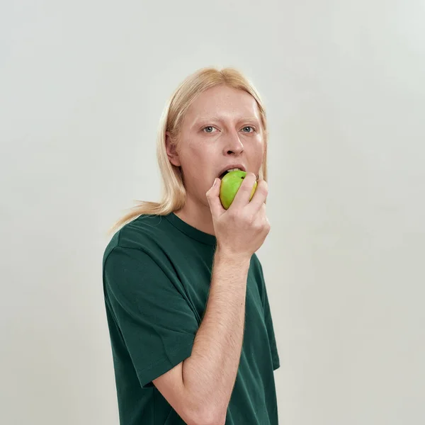 Şehvetli genç beyaz adam yeşil elma ısırıyor. — Stok fotoğraf