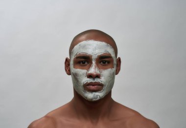 Yakışıklı Afro-Amerikalı adam kameraya bakıyor, siyah yüz maskesi kullanıyor, gri arka planda izole edilmiş poz veriyor.