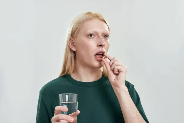 Молодой кавказский человек глотает таблетки с водой — стоковое фото