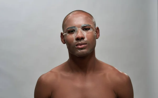 Portret van kalme jonge aantrekkelijke Afrikaanse Amerikaanse man met gezicht textiel vel masker kijken naar de camera, poseren geïsoleerd over grijze achtergrond — Stockfoto