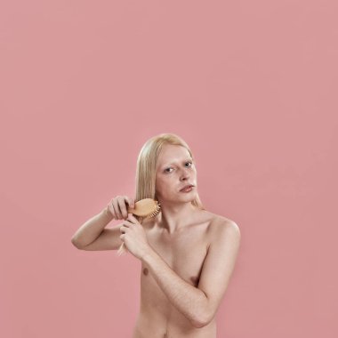 Genç beyaz adam uzun sarı saçlarını tarıyor.