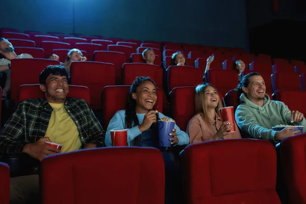 Um grupo de amigos felizes e diversos rindo enquanto assistem ao filme juntos, sentados no auditório de cinema — Fotografia de Stock