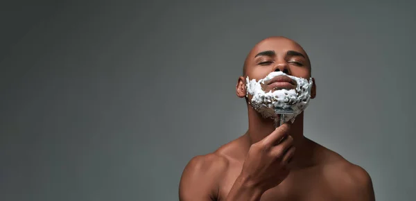 Retrato de jovem afro-americano sem camisa usando navalha de aço para remover restolho do pescoço, posando com os olhos fechados isolados sobre fundo cinza — Fotografia de Stock