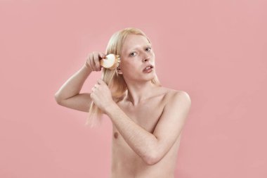 Genç beyaz adam uzun sarı saçlarını tarıyor.