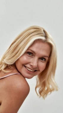 Orta yaşlı bir kadın omzunun üstündeki kameraya bakıyor.