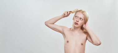 Genç üstsüz, zayıf, beyaz bir adam saçını tarıyor.