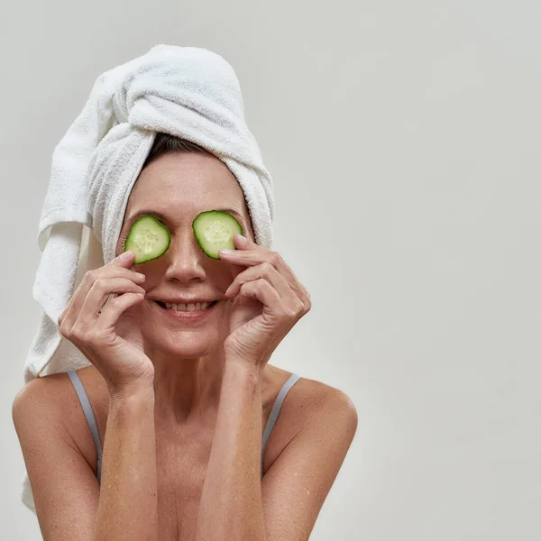 Kaukasische Frau mittleren Alters legt Gurkenscheiben auf die Augen — Stockfoto