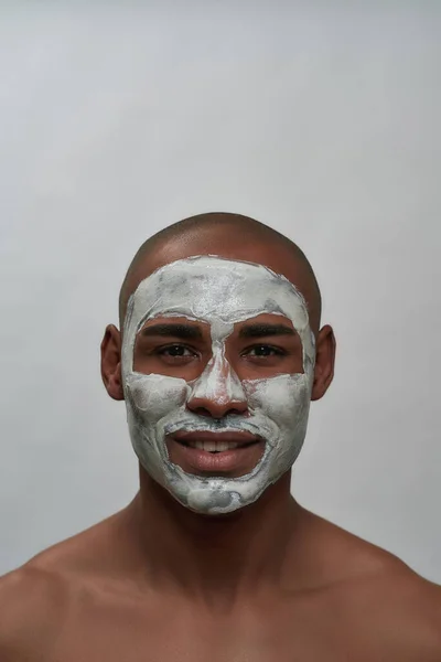 Handsome young african american man smiling at camera, using facial blackhead pore removal mask, posing isolated over gray background — Stock Photo, Image