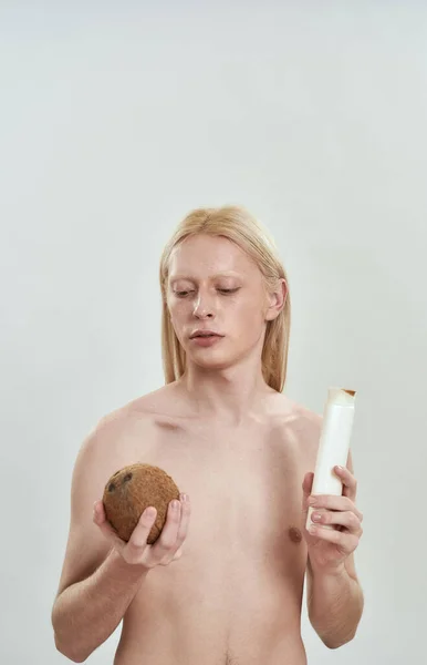 Junger Kaukasier mit Shampoo-Flasche und Kokosnuss — Stockfoto
