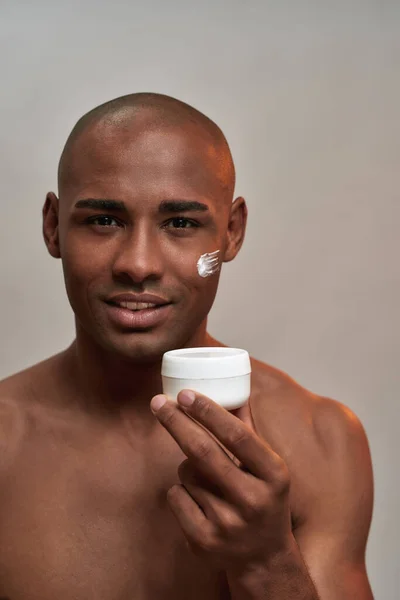 Cosmetica pot vastgehouden door multiraciale man met crème op het gezicht — Stockfoto