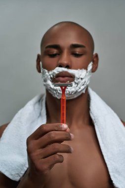 Gri arka planda izole edilmiş havluyla jiletle poz veren Afro-Amerikan genç adam.