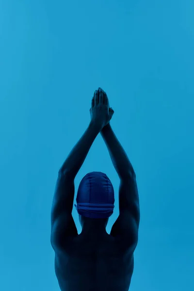 Jovem nadador. Tiro vertical de um adolescente africano em gorro de natação em pé em pose inicial isolado sobre fundo azul, pronto para mergulhar — Fotografia de Stock