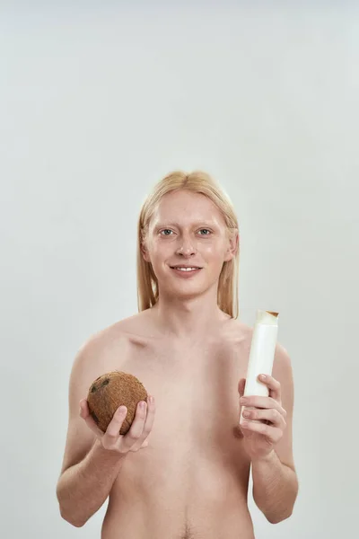 Jovem feliz segurando garrafa de xampu e coco — Fotografia de Stock