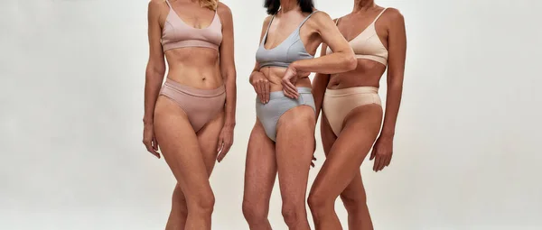 Concept de positivité corporelle. Plan recadré de trois femmes âgées en sous-vêtements posant à moitié nue en studio sur fond clair — Photo