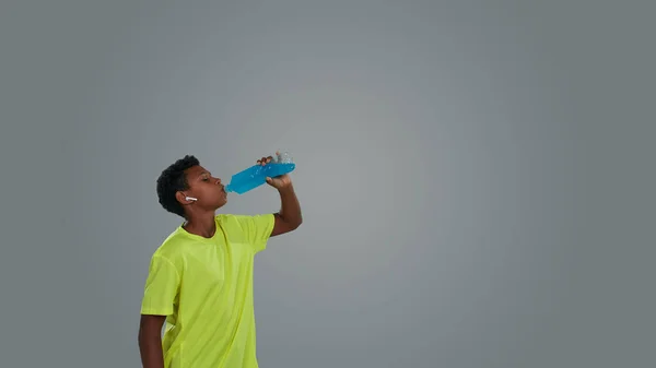 Dehydratation während körperlicher Aktivitäten. Seitenansicht eines sportlichen afrikanischen Teenagers, der vor grauem Hintergrund einen blauen Energy Drink trinkt — Stockfoto
