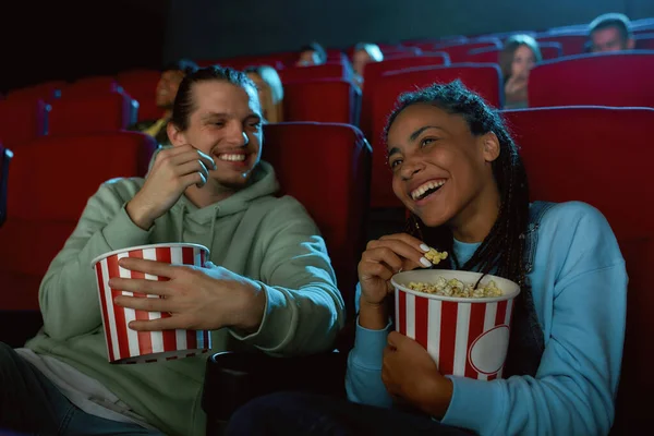 Joyeux jeune couple riant, ayant du pop-corn tout en regardant le film ensemble, assis dans l'auditorium du cinéma — Photo