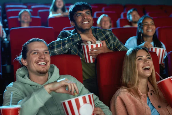 Joyful diverse people laughing while watching movie together, sitting in cinema auditorium