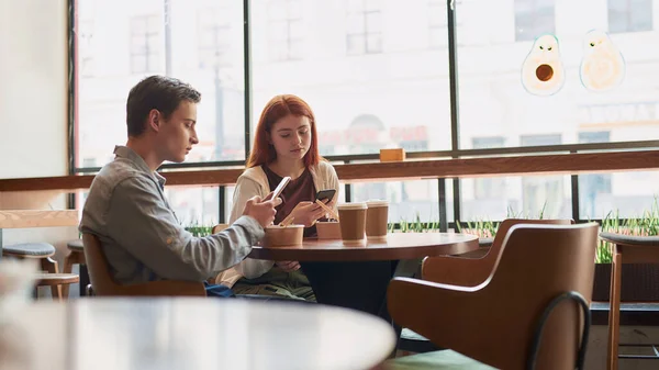 Para nastolatków całkowicie pochłonięta korzystaniem z telefonów, ignorując się nawzajem siedząc razem w kawiarni w ciągu dnia — Zdjęcie stockowe