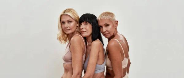 Belleza natural. Retrato de estudio de tres mujeres maduras felices en ropa interior posando juntas aisladas sobre fondo claro — Foto de Stock