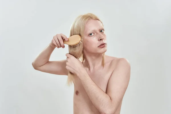 Young man grooming his long blond hair with comb — Stock Photo, Image