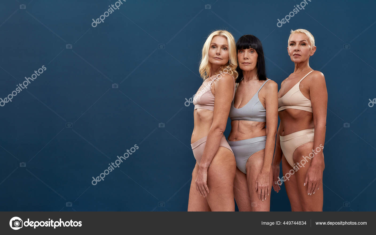 Three caucasian mature women in underwear looking at camera while posing half naked in studio against dark blue background Stock Photo by ©LanaStock 449744834 image