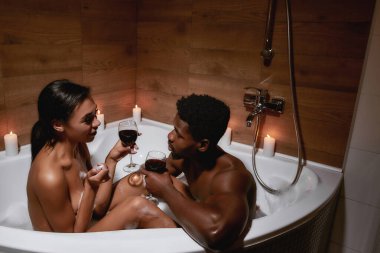 İlişkilerde samimiyet. Genç, çıplak, Afrikalı, şarap içen ve mumlarla banyo yaparken konuşan bir çift.