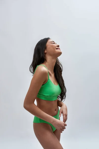 Joyeux jeune modèle féminin avec un corps mince parfait portant des sous-vêtements verts souriant tout en posant pour la caméra isolée sur fond clair — Photo
