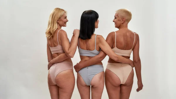 Three Attractive Middle Aged Women In Underwear Embracing Each Other While  Posing Together On Light Background Stock Photo, Picture and Royalty Free  Image. Image 165585072.