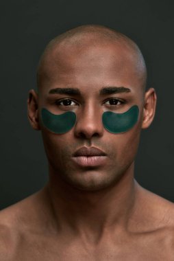 Göz bantları koyu yeşil olan ciddi bir adam.