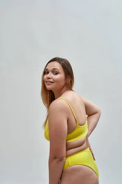 Caucasienne jeune femme portant des sous-vêtements jaunes tournant la tête à la caméra tout en posant isolé sur fond gris — Photo