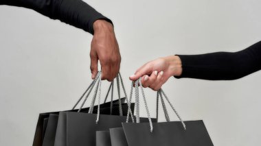 Kadın ve erkeğin elinde siyah kese kâğıdı tutarken yakın plan çekimleri. Aydınlık arkaplanda izole bir şekilde alışveriş yaptıktan sonra.