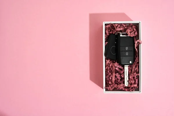 愛する女性への豪華な贈り物。パステルピンクの背景にギフトボックスの車のキーのトップビュー — ストック写真