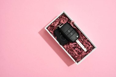 Onun için özel bir hediye. Pastel pembe arka planda beyaz kutuda bir araba anahtarının üst görünümü
