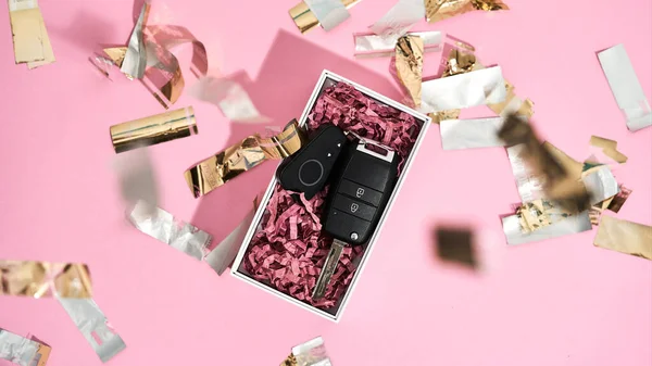 Het mooiste cadeau ooit. Close-up van een auto sleutel in geschenkverpakking en glanzende gouden confetti op pastel roze achtergrond — Stockfoto