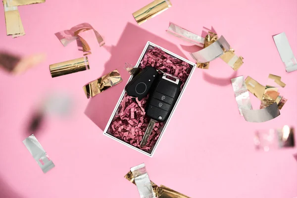 Bovenaanzicht van een autosleutel in geschenkverpakking en glanzende gouden confetti op pastel roze achtergrond — Stockfoto