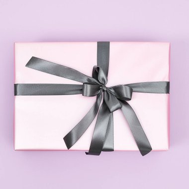 Kadınlar Günü 'nde onun için hediye. Mor arka planda gri fiyonklu pembe bir hediye kutusunun üst görüntüsü