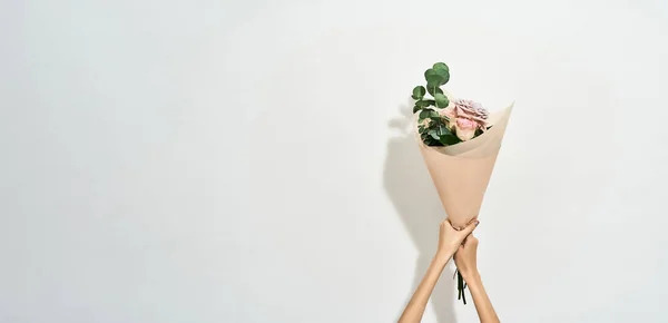 Gelukkige Vrouwendag. Vrouwelijke handen houden mooie bloemen boeket verpakt in ambachtelijk papier over lichte achtergrond — Stockfoto