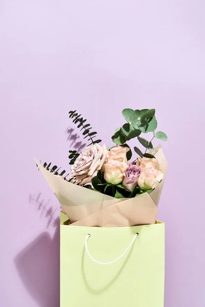 Mooie en verse bloemen boeket in papieren geschenkzak over paarse achtergrond, verticaal schot — Stockfoto