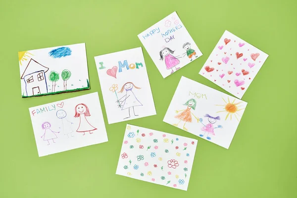 For the best mom in the world. Top view of colorful child drawings with colored pencils for mothers day on green background, handmade greeting card from child