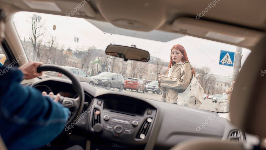 Male driver honking the horn in the car while distracted teenage girl using her mobile phone, crossing the street. Technology and transportation concept